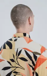Camisa de manga larga con cuello y botones frontales, confeccionada en rayón con un estampado de hojas tropicales en tonos beige, naranja, negro y verde oliva.