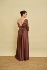 Vestido largo color marrón de silueta fluida, con escote en V pronunciado, mangas tres cuartos de tul con detalles sutiles, nudo drapeado en el centro del pecho y tajo delantero en la falda.