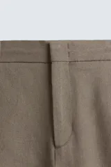 Pantalón de calce relajado confeccionado en tejido de viscosa y yute color tostado. Presenta cintura elástica ajustable con cordón, bolsillos laterales, bolsillos traseros de vivo y cierre frontal con cremallera y botón.