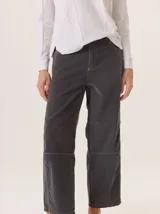 Pantalón de pana color gris oscuro, de corte barrel (holgado en caderas y muslos, ligeramente afín hacia el tobillo). Presenta costuras visibles en contraste de color amarillo claro, especialmente en la zona de la rodilla y el ruedo.