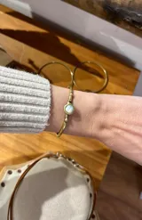 Pulsera rígida de bronce ajustable a presión, con una piedra circular central de nácar y detalles abultados en el metal.
