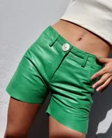 Shorts de cuero color verde de tiro medio y corte recto, con cierre frontal, botón y bolsillos funcionales.