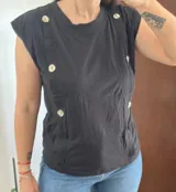 Musculosa negra sin mangas, con hombreras, escote redondo y detalle de filas de botones decorativos nacarados en la parte frontal.