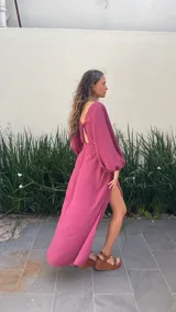 Vestido largo color bordó con escote en V profundo, detalle de nudo central y aberturas laterales en la cintura. Presenta mangas largas abullonadas con puños elásticos y falda con tajo frontal pronunciado.
