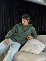 Canguro verde oliva con capucha y cordones ajustables. Estampado en la espalda con la frase "Bad Ideas Good Stories" en letras azules.