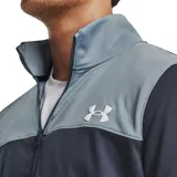 Conjunto deportivo Under Armour compuesto por una campera con cierre frontal y cuello alto, y un pantalón de jogging a juego. La campera presenta un diseño bicolor con la parte superior en gris y el resto en azul marino, mientras que el pantalón es de color azul marino. Ambas piezas incluyen el logo de la marca estampado en blanco.