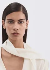 Blusa de modal y poliéster color blanco marfil, con diseño recto, escote en V, mangas largas y detalle de fular incorporado en el cuello. Cierre frontal con botones.