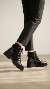 Bota corta de cuero negro con diseño versátil que incluye una pieza frontal removible con cierre y detalles de tachas metálicas. Presenta una combinación de texturas en cuero liso y cuero con textura tipo reptil en el talón, con suela track de goma.