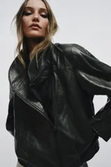 Chaqueta de corte amplio estilo biker en tejido efecto piel de color verde oscuro, con cuello alto envolvente, cierre frontal asimétrico de cremallera metálica, bolsillos ocultos en costura y forro interior.