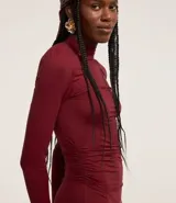 Vestido midi color bordó, de microfibra ligera, con cuello alto fruncido, manga larga, hombreras y detalle fruncido lateral.