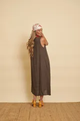 Vestido midi de lino color marrón, sin mangas y con escote en V. Presenta detalles de flecos a lo largo de la abertura y una franja bordada con lentejuelas en el ruedo. Incluye bolsillos laterales.