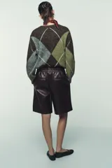 Bermuda de tiro alto confeccionada en material efecto piel, con cintura elástica y costuras verticales decorativas en el frente.