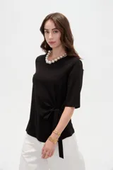 Remera negra de manga corta, con cuello redondo y diseño holgado con detalle de lazo para anudar en la cintura.