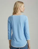 Remera de modal color blanco, con cuello redondo y mangas 3/4. Presenta un aplique bordado en color tostado en el cuello, los puños y el ruedo.