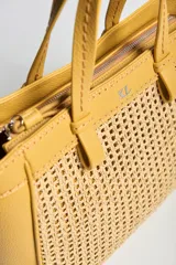 Cartera tipo tote color amarillo con detalles en textura tejida en la parte frontal y trasera, asas de mano y correa de hombro ajustable y desmontable. Incluye aplique metálico con el logo de la marca.