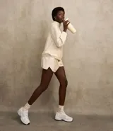 Short deportivo color beige, modelo runner, confeccionado en poliamida, con cintura elástica y lazo. Presenta recortes con hilo reflectante y un bajo redondeado.