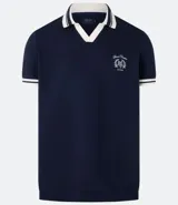 Remera polo comfort color crudo, de manga corta con ribete verde y cuello en V con ribete verde. Tiene un pequeño logo bordado en el pecho.