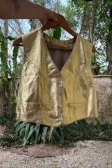 Chaleco dorado de cuero napa con cuello en V, cierre frontal con botones y dos bolsillos de parche.