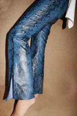 Pantalón de cuero con estampado de serpiente en tonos amarillos y negros, de corte recto y tiro medio. Presenta bolsillos delanteros aplicados en contraste de color y aberturas en el bajo.