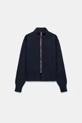 Chaqueta de punto color azul marino, de cuello alto y manga larga, con cierre frontal de cremallera metálica y detalle de abertura en el bajo delantero.