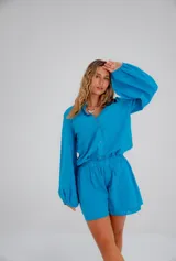 Conjunto de dos piezas confeccionado en lino color blanco. Incluye una camisa de corte holgado con mangas abullonadas y bolsillos frontales, y un short de tiro alto con cintura elástica y forro interior.