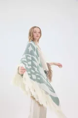 Ruana de punto triangular tejida en lambswool, con diseño geométrico en tonos tostado, blanco y negro, terminada con flecos en los bordes.