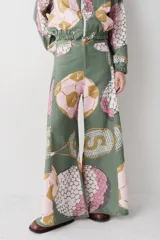 Pantalon de corte wide leg con tiro alto, confeccionado en tela con estampado integral de motivos deportivos como pelotas de golf, pelotas de futbol y raquetas de tenis sobre fondo verde.