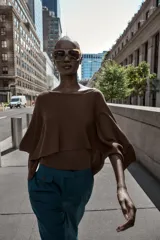 Pantalón de vestir marrón oscuro, tiro alto, con pernera ancha y pinzas frontales. Presenta un bolsillo con tapeta en la parte superior delantera.