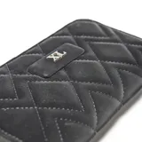 Billetera rectangular tipo fichero color negro, con diseño acolchado de costuras en forma de rombos y cierre perimetral. Presenta una placa metálica frontal con el logo XL.