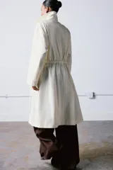 Trench oversize de cuello solapa y manga larga, con cintura ajustable mediante cordones y cierre frontal oculto. Cuenta con bolsillos laterales y forro interior.