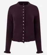 Cardigan de punto color bordó con cuello redondo, cierre frontal de botones de nácar y detalle de volados en la tapeta de botones y el ruedo. Presenta mangas largas con puños ajustados.