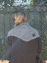 Bufanda de punto con diseño triangular en color marrón oscuro, con detalle de etiqueta de cuero sintético en una esquina.
