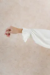 Blusa color crema de tela tejida 100% lana, con cuello fruncido y mangas largas con puños elásticos.