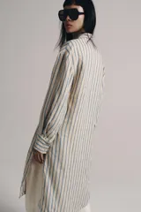 Vestido midi estilo camisero de Zara Woman Collection, confeccionado en lino, con estampado de rayas verticales azules sobre fondo beige. Cuenta con cuello solapa, escote en V con botonadura parcial, manga larga con puños abotonados, un bolsillo de plastrón en el pecho y bajo redondeado.
