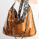 Bolso bandolera de cuero color marrón con detalles en negro. Tiene dos bolsillos con cierre en la parte trasera, cierre superior y forro interior con bolsillo con cierre y bolsillo para el móvil. Incluye dos correas removibles: una de cuero ajustable y otra de cadena.