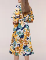 Vestido midi de calce holgado y caída fluida con escote en V cruzado, cintura elastizada fruncida y mangas cortas con volados superpuestos. Cuenta con un diseño estampado de flores grandes en tonos amarillo, blanco, azul marino y verde.