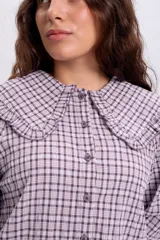 Camisa de manga larga con estampa a cuadros en tonos violeta y blanco, con cuello babero amplio con volados y cierre frontal abotonado.