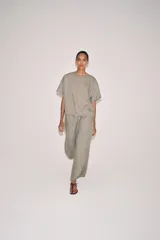 Top de lino de color beige, con cuello redondo, manga corta, bolsillos frontales aplicados y bajo ajustable con cordones. Cuenta con abertura en la espalda y cierre de botón.