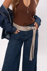 Faja de cuero gamuzado metalizado color visón, con curvatura anatómica, herraje metálico plateado y tiras largas con flecos para atar en nudo.