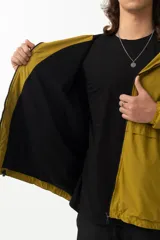 Campera de nylon color mostaza, estilo 'gorpcore', con forro de jersey de algodón y corte confortable. Presenta cierre frontal, capucha y bolsillos laterales. Estampado en el pecho con el logo de la marca y la frase "Release the hounds".