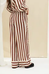Pantalón largo de corte ancho, con diseño de rayas verticales en colores marrón y blanco, cintura elástica con cordón de ajuste y detalles de franjas horizontales en el ruedo.