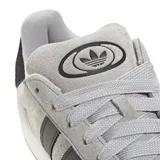 Championes Adidas modelo Campus 00s, confeccionados en gamuza gris con las icónicas tres tiras laterales en negro. Presentan un diseño de inspiración retro con suela de goma blanca y base color caramelo, cordones gruesos y detalle de marca en el talón y lateral.