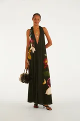 Mono palazzo largo de color negro con estampado de maxi orquídeas coloridas, escote en V pronunciado y tirantes halter que se atan al cuello. Presenta un diseño holgado y fluido.