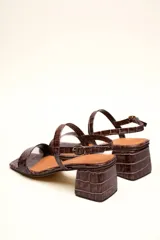 Sandalia de cuero vacuno color negro con textura de cocodrilo, taco cuadrado de 4 cm, punta cuadrada y dos tiras finas, una en el empeine y otra con hebilla en el tobillo.