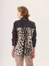 Camisa de manga larga con diseño combinado. Presenta mangas y parte superior delantera y trasera en color negro liso, mientras que el panel central de la espalda destaca por un estampado animal print de leopardo. Cuenta con cuello clásico, cierre frontal de botones y puños abotonados.