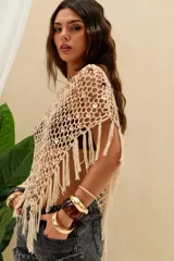 Top corto tejido en crochet de color crudo, con diseño de red adornado con lentejuelas y flecos colgantes en el dobladillo. Presenta un corte asimétrico de un solo hombro.