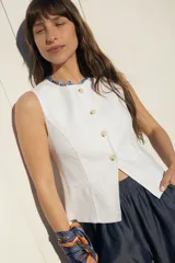 Chaleco sastrero blanco sin mangas, con cuello redondo y cierre frontal de botones con efecto carey. Presenta bolsillos ojal simulados en la parte inferior.