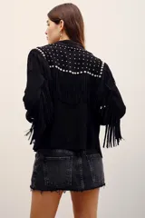 Camisa de gamuza negra con mangas largas, flecos y aplicación de tachas metálicas plateadas en la parte frontal y en los hombros.