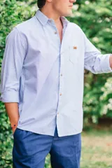 Camisa de manga larga con diseño de rayas finas celestes y blancas, cuello camisero, botones de madera y un bolsillo frontal en el pecho con detalle de aplique de marca.