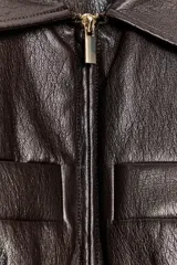 Chaqueta de efecto piel con cuello solapa, manga corta y cintura elástica. Presenta cierre frontal con cremallera y bolsillos decorativos en el frente.